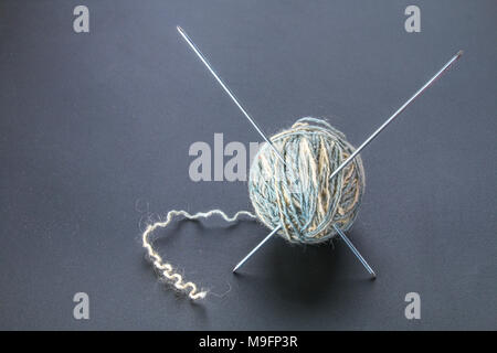 Une balle de laine avec des aiguilles à tricoter et de chaussettes sur un tableau gris. La couture Banque D'Images