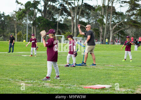 Un adulte utilise un pitching machine pitching suivantes bien qu'avec une action de bras au junior de softball. Banque D'Images