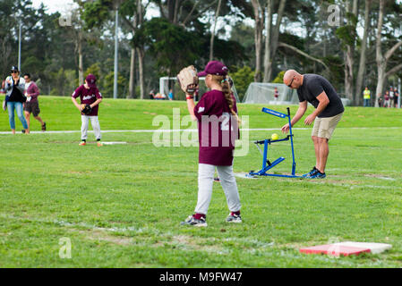 Un adulte utilise un pitching machine pitching suivantes bien qu'avec une action de bras au junior de softball. Banque D'Images