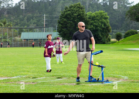 Un adulte utilise un pitching machine pitching suivantes bien qu'avec une action de bras au junior de softball. Banque D'Images