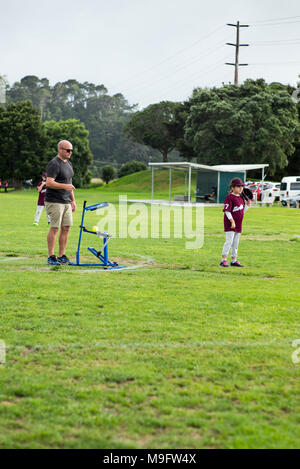 Un adulte utilise un pitching machine pitching suivantes bien qu'avec une action de bras au junior de softball. Banque D'Images