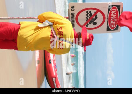 Un membre Surf Rescue se tient à côté du signe de danger lorsqu'il regarde les nageurs dans l'eau, Gold Coast, Queensland, Australie Banque D'Images