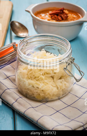 Soupe de choucroute cuisine tchèque avec de la saucisse et les pommes de terre dans un plat blanc sur bleu table bois Banque D'Images