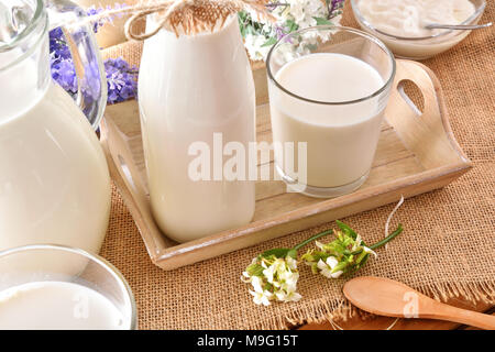 Le lait contenant le tissu de toile cirée sur la table en bois avec bac et fleurs décoratives. Composition horizontale. Elevated view Banque D'Images