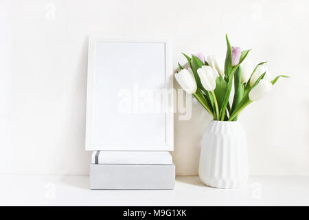 Cadre en bois blanc vide avec la maquette spring bouquet de tulipes dans un vase en porcelaine et pile de livres se trouvant sur la table. Poster design de produits, tyled sto Banque D'Images