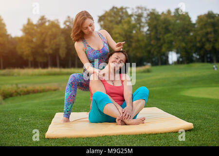Portrait de deux femmes faisant le massage thaïlandais. Femme assise sur mat. Parc d'été. Banque D'Images