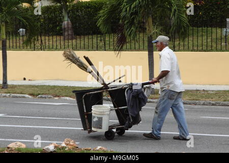 Un homme pousse un panier en face de lui. Le panier a mis des conteneurs à ordures dans et les ustensiles tels que le balai. Banque D'Images