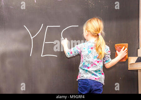 Cute little girl écrit oui sur tableau dans une salle de classe Banque D'Images