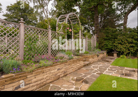 Chemin, plantes à fleurs sur border, pelouse, mur de pierre, de treillis en bois arch & écran - beau, conçu, aménagé, le jardin - West Yorkshire, Angleterre. Banque D'Images