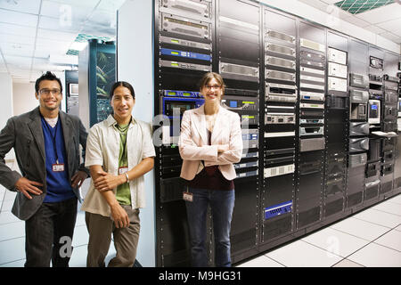 Portriat de trois muli-ethnique les techniciens qui travaillent dans une grande salle de serveurs informatiques. Banque D'Images