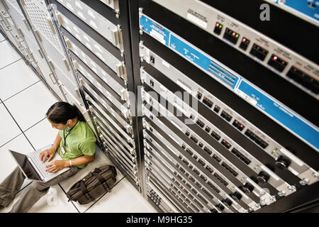 Technicien en informatique travaillant sur un portable tout en faisant le travail de diagnostic sur un serveur dans une plus grande salle de serveurs informatiques. Banque D'Images