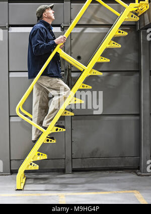 Warehouse worker climbing un escalier métallique dans un entrepôt pour l'eau en bouteille. Banque D'Images