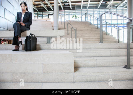 Hispanic businesswoman sitting on stairs dans le hall d'un grand immeuble de bureaux. Banque D'Images