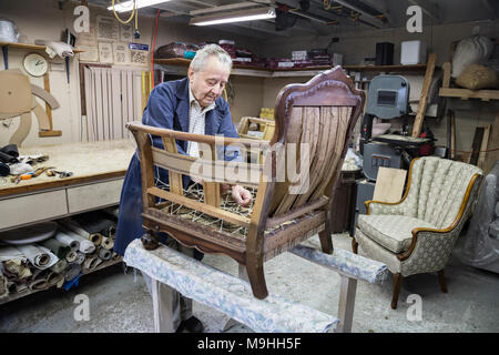 Young man rembourreur travaille sur une scène musicale antigue président dans son garage boutique. Banque D'Images