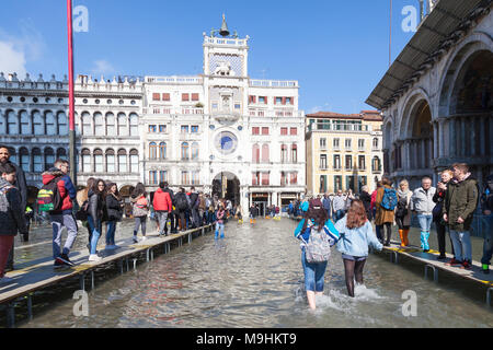 Deux femmes pieds nus par éclaboussures Acqua Alta inondations, la Piazza San Marco, Venise, Italie regardés par les personnes marchant sur vers le Réveil T passarelles Banque D'Images