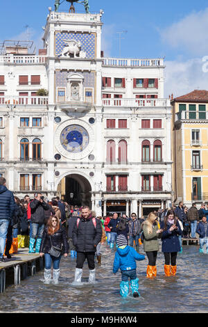 Les touristes patauger par Acqua Alta marée haute en face de la tour de la cloche sur la Piazza San Marco (Place Saint Marc), Venise, Vénétie, Italie en plas colorés Banque D'Images