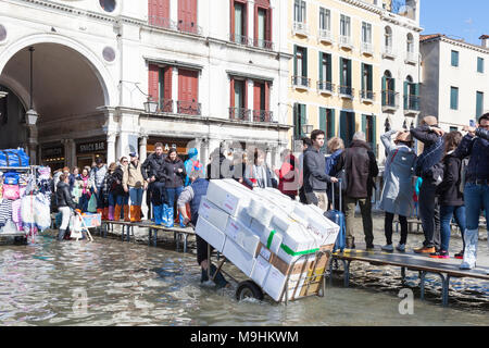 Un travailleur avec un chariot de livraison dans les inondations acqua alta , Piazza San Marco (Place Saint Marc), Venise, Italie passant personnes marchant sur passarell Banque D'Images