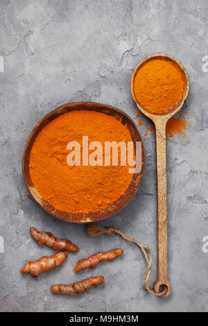 Le curcuma en poudre dans un bol de noix de coco, le curcuma racines sur un fond de béton gris. Vue de dessus Banque D'Images