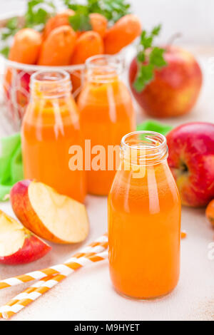 La carotte fraîche et du jus de pommes sur fond blanc. La carotte et le jus de pomme dans des bouteilles en verre sur le tableau blanc, gros plan Banque D'Images