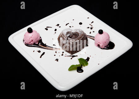 Fondan dessert au chocolat avec de la glace sur une plaque blanche sur fond noir. Français exquis fondan au chocolat. Banque D'Images