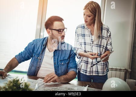 Jeune architecte pensif colleagues talking et analyser les bleus tout en travaillant sur un nouveau projet sur la tablette numérique à l'office. Banque D'Images