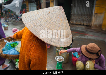 Vietnam Hat Woman, vue arrière d'une femme portant un chapeau conique typiquement vietnamien discutant avec un vendeur de rue dans le marché de Hoi an, au centre du Vietnam. Banque D'Images