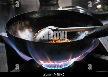 Frire la viande avec riz Chef sur la cuisinière à gaz avec le feu à la cuisine, le chef au travail, pot au feu. La cuisson sur un brûleur au gaz. bleu flamme de feu autour de Banque D'Images