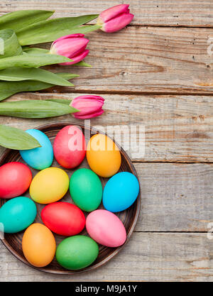 Les oeufs de Pâques colorés et des tulipes sur fond de bois Banque D'Images