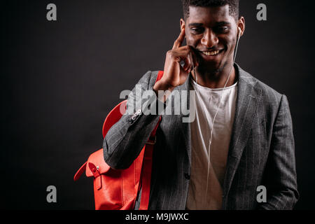 Heureux étudiant africain dans une ambiance décontractée et la broche clothers bag l'apprentissage de la langue russe sur les écouteurs. stydy utiles temps libre. Banque D'Images