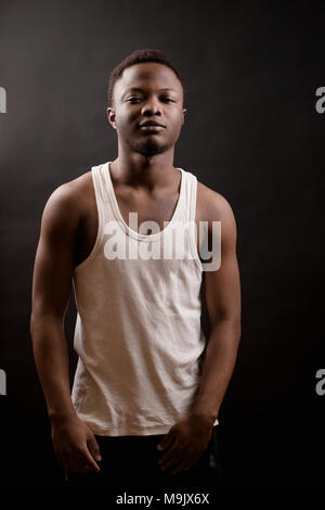 Athlète brutal de l'Afrique debout dans clothers occasionnels sur le fond noir. homme fort. jogger Banque D'Images
