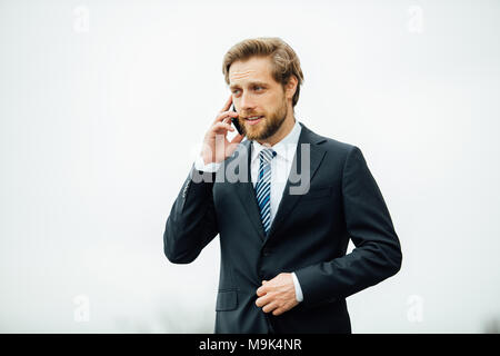 Homme d'affaires en costume élégant ayant une belle présentation sur téléphone mobile, quelque part dans la rue entre les réunions d'affaires Banque D'Images