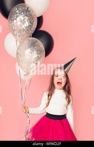 Petit enfant anniversaire girl studio isolé sur fond rose holding balloons cris surpris Banque D'Images