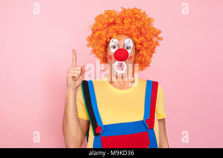 L'homme à une perruque rouge, bretelles et le maquillage ont une grande idée. Clown, corcus ou show concept. Fond rose, Studio shot Banque D'Images
