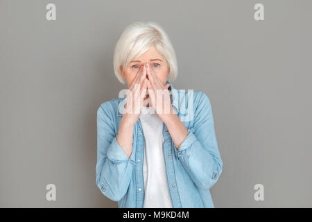 Des femmes plus âgées portant des jeans jacket studio isolé sur fond gris, les éternuements attrapé un rhume à la sensation de malaise de l'appareil photo Banque D'Images