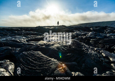 Un homme marche sur la plaine côtière ancienne coulées volcaniques comme VOG (smog) à partir d'un hotspot actif par dérive dans la distance, Hawaii Volcanoes Nation Banque D'Images