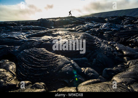 Un homme marche sur la plaine côtière ancienne coulées volcaniques comme VOG (smog) à partir d'un hotspot actif par dérive dans la distance, Hawaii Volcanoes Nation Banque D'Images