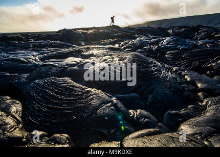 Un homme marche sur la plaine côtière ancienne coulées volcaniques comme VOG (smog) à partir d'un hotspot actif par dérive dans la distance, Hawaii Volcanoes Nation Banque D'Images