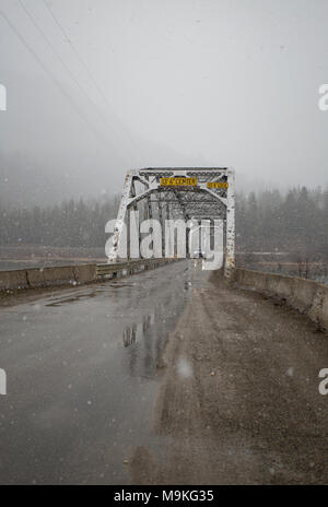 Une voiture en traversant l'une voie Noxon truss steel pont sur la rivière Clark Fork sur une chaussée mouillée, jour de neige. La Noxon pont a été construit d'un acier, nin Banque D'Images