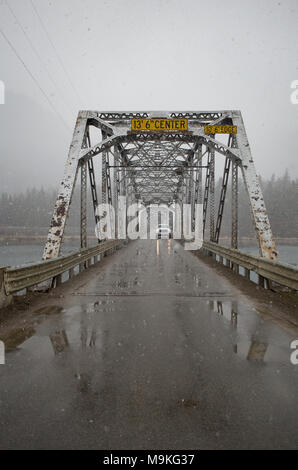 Un camion traversant la une voie Noxon truss pont en acier sur la rivière Clark Fork sur une chaussée mouillée, jour de neige. La Noxon pont a été construit d'un s Banque D'Images