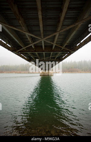 Vue du dessous du pont d'acier en treillis Noxon sur la rivière Clark Fork sur une chaussée mouillée, jour de neige. Banque D'Images