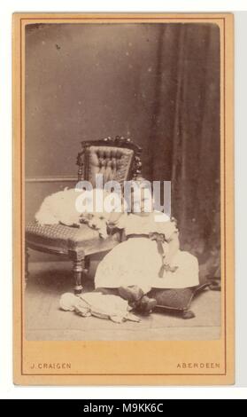 Portrait de studio victorien, carte de visite (carte de visite) d'une jeune écossaise assise portant son meilleur party frock, en apparence pétulante, stramppy, tandis que son Cairn ou West Highland terrier est assis sur la chaise, 1860's, Aberdeen, Écosse, Royaume-Uni Banque D'Images