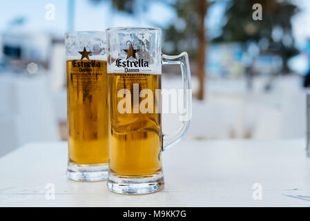 Corralejo, Fuerteventura, Îles Canaries, Espagne - 16 Février 2018 : deux pots de bière Estrella Damm froide contre l'arrière-plan flou tropical Banque D'Images