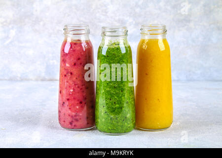 Vert, jaune, violet smoothies en bouteilles de fruits rouges, verts, oranges sur un tableau blanc sur un tableau gris Banque D'Images
