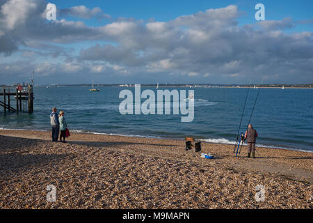 Deux personnes regardant un bateau se déplaçant le long de la Solent dans la Manche, à partir de la plage de Calshot UK alors qu'un pêcheur met en place des prêts pour une journée de pêche Banque D'Images