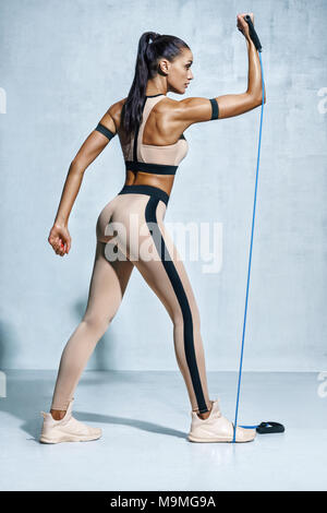 Woman exercising with resistance band. Photo de femme sportive dans les vêtements de sport d'entraînement sur fond gris. Force et motivation Banque D'Images