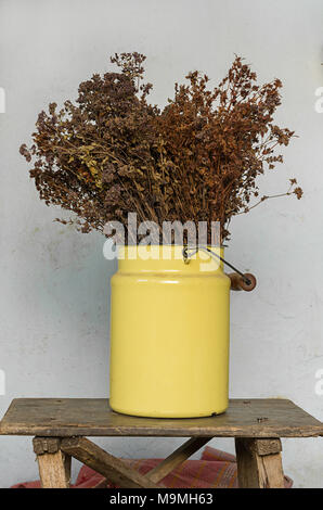 Décoration maison concept : prairie séchées des fleurs dans un pot en métal jaune sur le vieux banc de bois avec des clous qui sort Banque D'Images