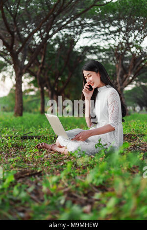 Belle femme à l'aide d'ordinateur portable et d'appeler avec un téléphone mobile dans le parc extérieur Banque D'Images