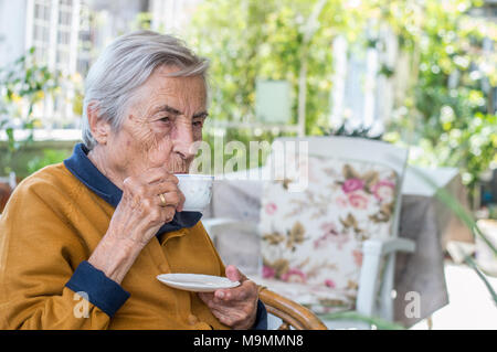 Femme âgée assis et boire le café turc dans le balcon sur une journée ensoleillée. Banque D'Images