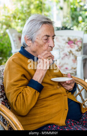 Femme âgée assis et boire le café turc dans le balcon sur une journée ensoleillée. Banque D'Images