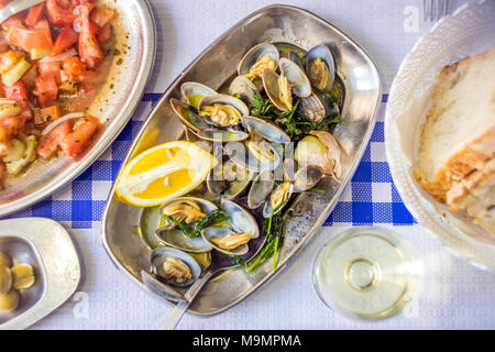 Table couverts avec les palourdes délicieux servi sur de l'argenterie, vin blanc, pain, salade de tomates et olives d'au-dessus, Portugal Banque D'Images